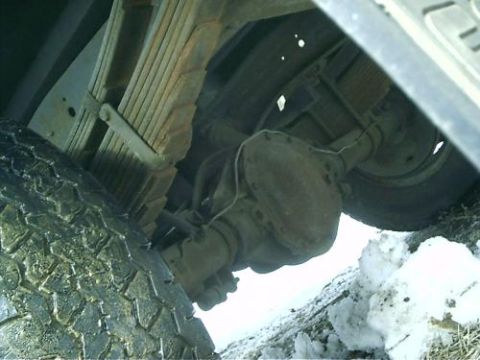 1979 Ford Bronco - The underside of a vehicle reveals its rear axle and suspension components, partially covered by snow.