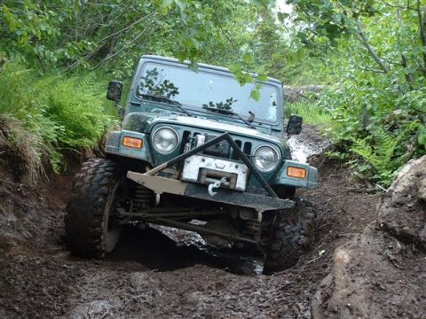 2000 Jeep TJ - A green Jeep Wrangler navigates a challenging muddy off-road path.