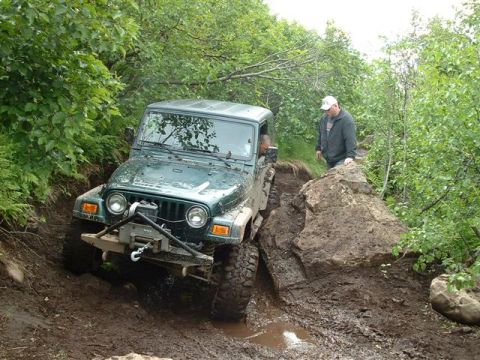 2000 Jeep TJ - A green 2000 Jeep TJ tackles a challenging muddy trail during an off-road event.