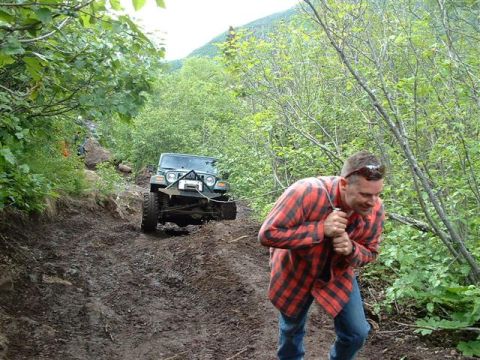 2000 Jeep TJ - A man pulls a rope attached to a green Jeep navigating a challenging muddy trail during an off-road event.