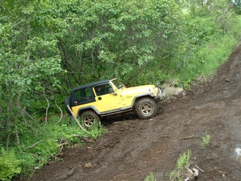 2000 Jeep Wrangler - A yellow Jeep Wrangler navigates a steep, muddy trail during an off-road excursion.