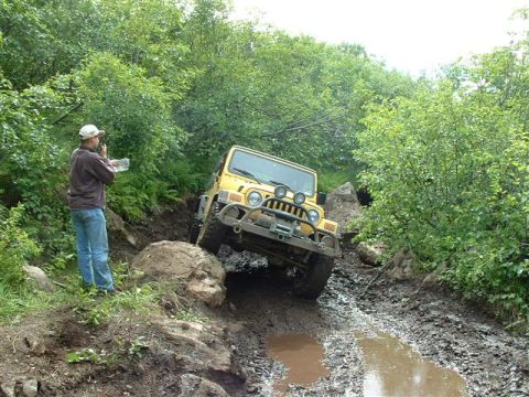 2000 Jeep Wrangler - A yellow Jeep Wrangler tackles a challenging muddy off-road path during an outing.