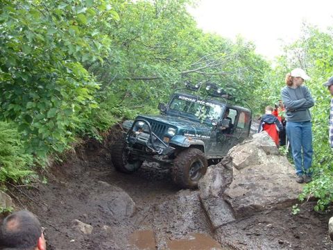 2000 Jeep Wrangler - A Jeep Wrangler tackles a challenging muddy obstacle during an off-road event.