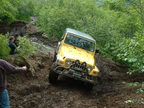 2000 Jeep Wrangler - A yellow Jeep TJ tackles a challenging muddy incline during an off-road excursion.