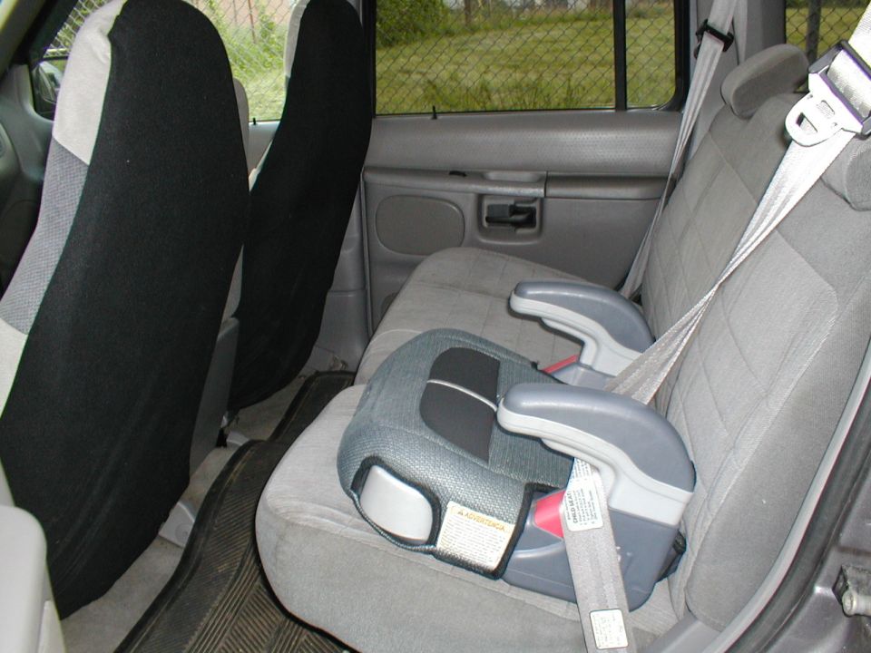 Vehicle interior showing gray seats, black seat covers, and a child car seat secured by a seatbelt