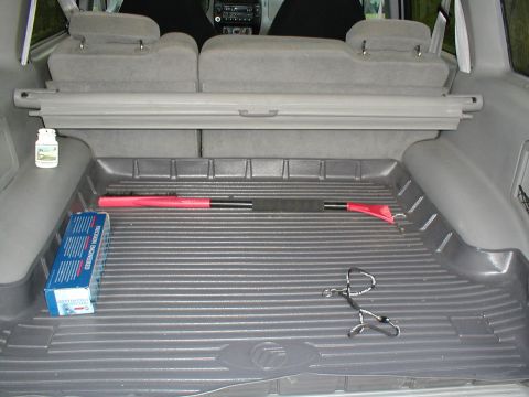 1979 Ford Bronco - The cargo area of a vehicle contains various items, including an ice scraper and a box of medication.