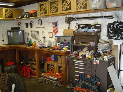 1989 Ford Bronco - A cluttered garage workbench is filled with tools, supplies, and storage, with Home Depot boxes stacked on a shelf above.