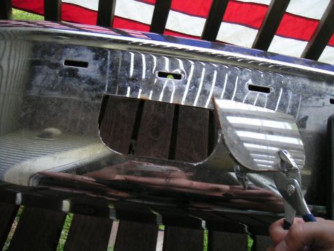1994 Ford Bronco - A chrome bumper is modified with cutouts, showing wooden planks underneath. Pliers are attached to a piece of metal.