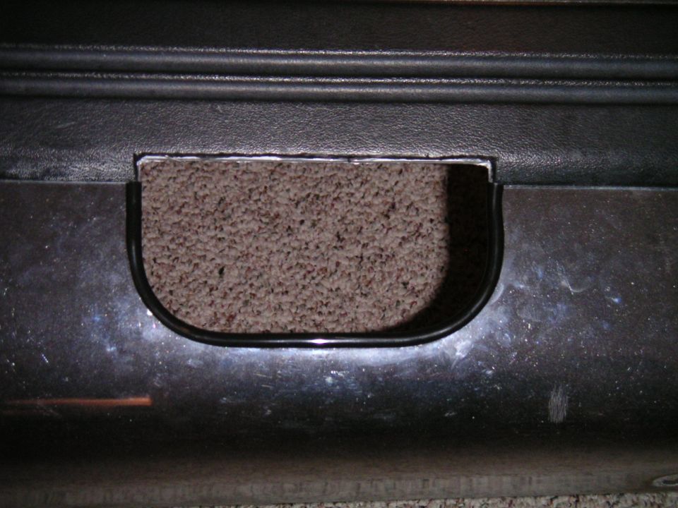 cutout in black plastic panel, carpet visible behind it