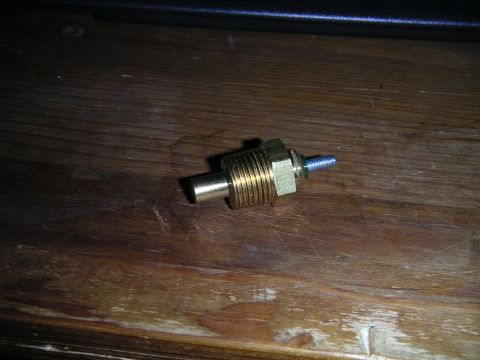 1994 Ford Bronco - A brass temperature sending unit with a threaded shaft and hex nut is shown on a wooden surface.