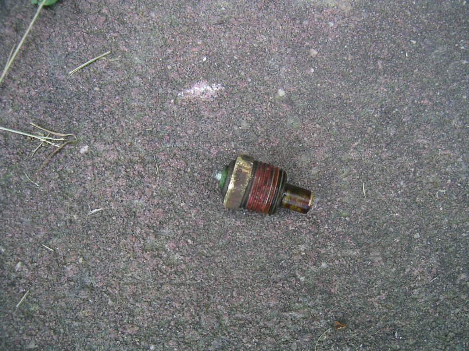 Corroded brass sensor with rust-stained threads lying on gravel