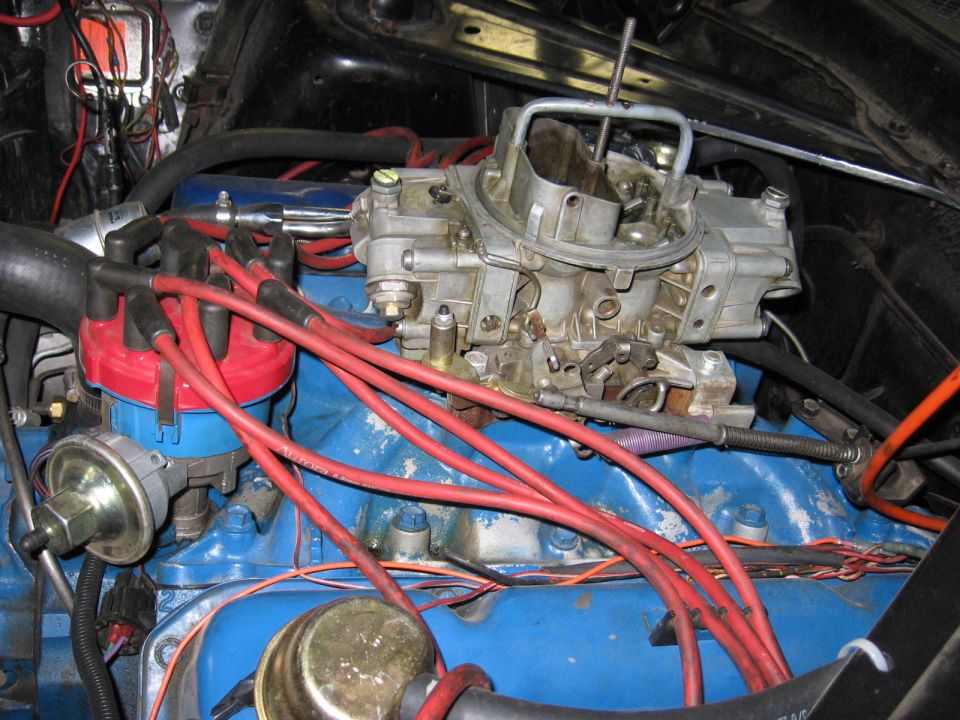 Close-up of a V8 engine bay showing a Holley carburetor, red spark plug wires, and a blue distributor cap