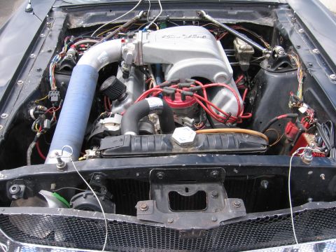 1972 Ford Mustang - The engine bay of a 1972 Ford Mustang, a V8 engine with a prominent intake system and red spark plug wires.