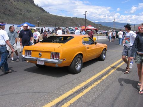 1972 Ford Mustang - A classic orange muscle car is seen from the rear on a sunny day at an outdoor event.