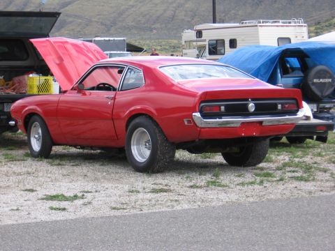 1972 Ford Mustang - A red coupe with its hood open is parked on a gravel lot next to other vehicles and RVs.
