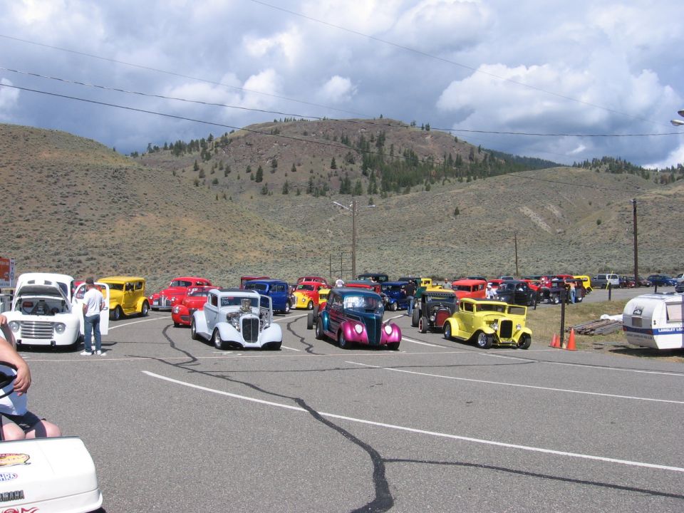 Many classic cars parked in a lot with hills in the background