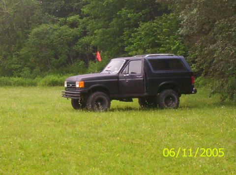 1995 Ford Bronco - A black Ford Bronco is parked in a grassy field with trees in the background.