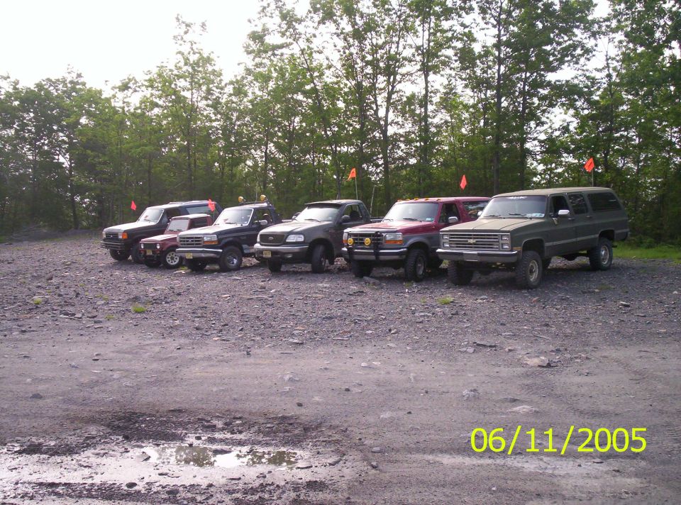 Row of off-road trucks and SUVs with orange trail flags in a gravel lot