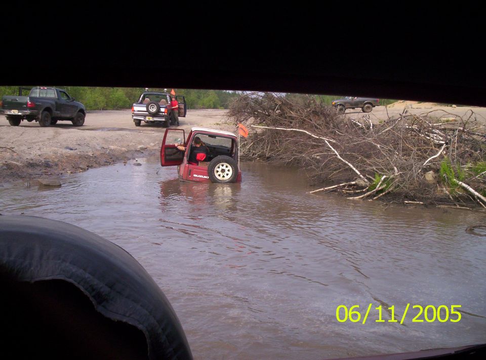 Red Suzuki Samurai stuck door-deep in muddy water at an off-road pit, 2005 date stamp