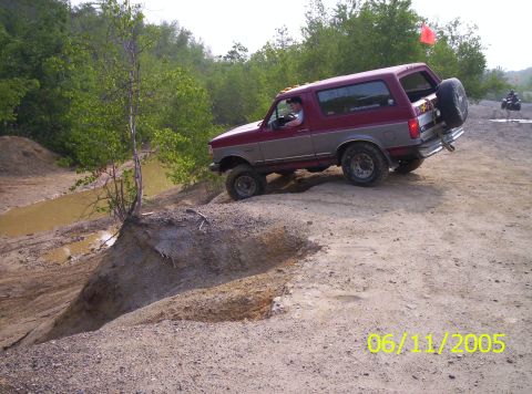 1995 Ford Bronco - Maroon and silver two-tone full-size Bronco with a white hardtop climbing out of a sandy pit at an off-road park, driver leaning out the wi…