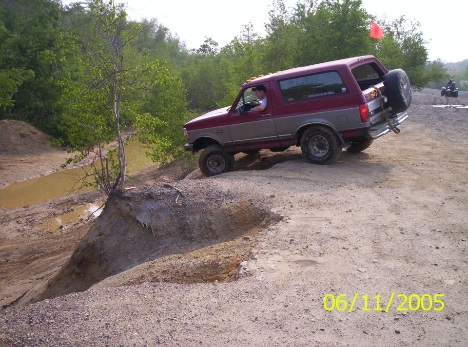 Maroon and silver Ford Bronco with white top climbing sandy off-road pit on mud tires