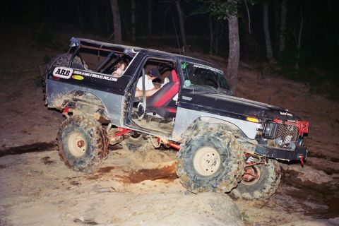 1978 Ford Bronco - This heavily modified SUV is navigating a challenging off-road course in a wooded area after dark.