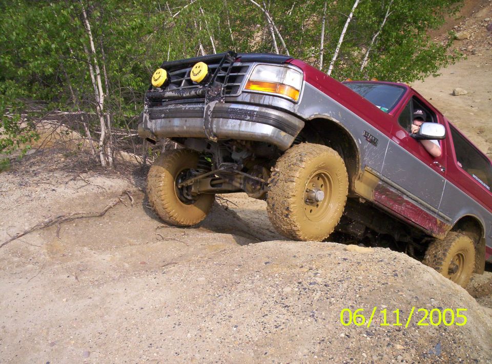 Two-tone Ford Bronco climbing a rock ledge with a front tire in the air, mud tires