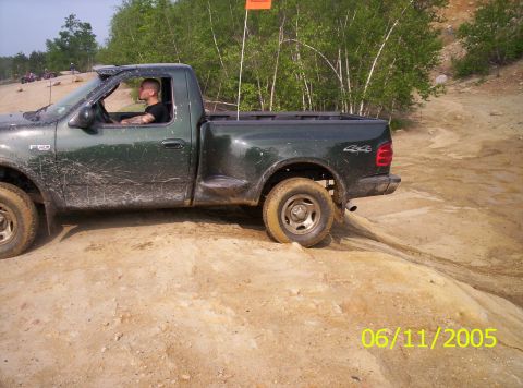 1995 Ford Bronco - Dark green regular-cab short-bed Ford F-150 4x4 seen in profile from the driver's side, working across a sandy rock ledge at an off-road pa…