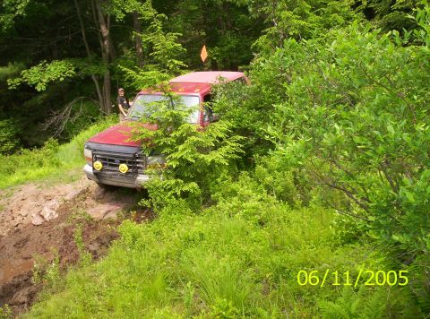 1995 Ford Bronco - Red 1995 Ford Bronco navigates a challenging off-road path surrounded by dense foliage.