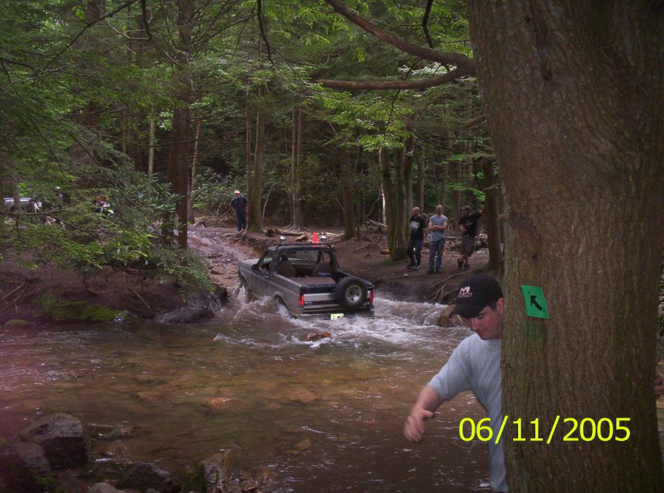 Gray 1995 Ford Bronco driving through a stream with people watching