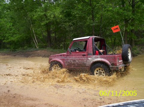 1995 Ford Bronco - Off-road vehicle navigating a muddy trail with trees in the background.