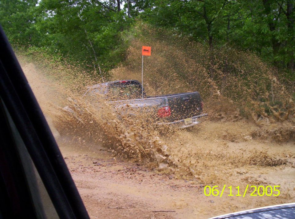 Truck driving through a mud puddle, kicking up a lot of water and mud