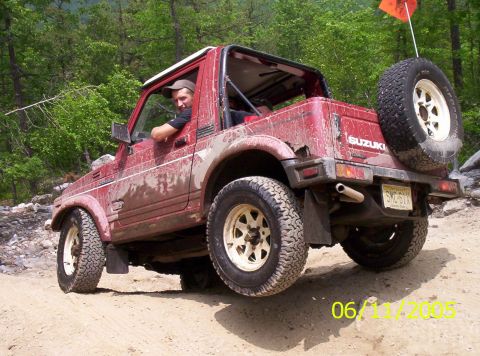 1995 Ford Bronco - A mud-splattered red Suzuki Samurai with the soft top removed, white spoke wheels, BFGoodrich all-terrain tires, a swing-out tire carrier w…