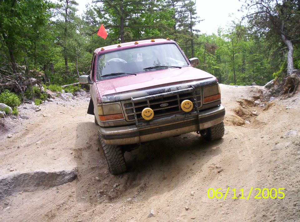 Maroon lifted Ford SUV with smiley-face light covers on rutted dirt trail