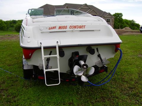 1997 Crownline 266 CCR - The rear view of a white boat on a trailer shows its propeller and a retractable ladder.