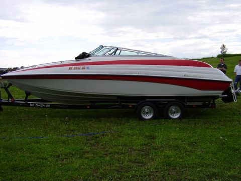 1997 Crownline 266 CCR - A white and red boat with a red stripe is parked on a trailer on a grassy field.