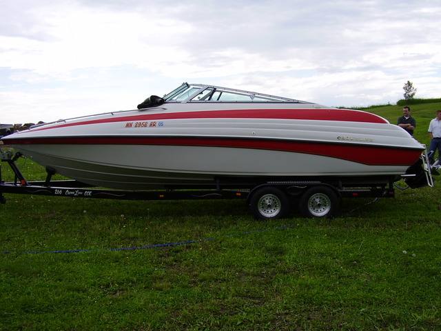 Red and white bowrider boat on trailer, side view on grass