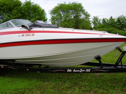 1997 Crownline 266 CCR - A white boat with a red stripe is parked on a trailer on a grassy area.