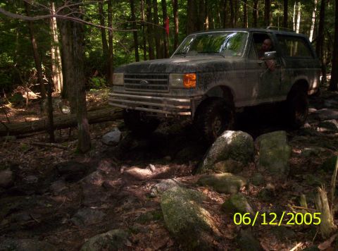1995 Ford Bronco - Ford Bronco driving through a forest with large rocks on the path.
