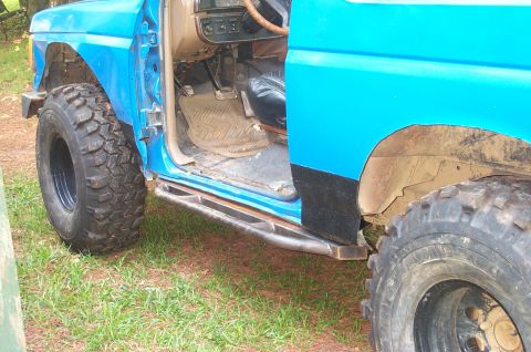 1987 Ford Bronco - The interior of a blue SUV is visible with the driver's door open, revealing the floor mats and pedals. Large off-road tires are mounted on…