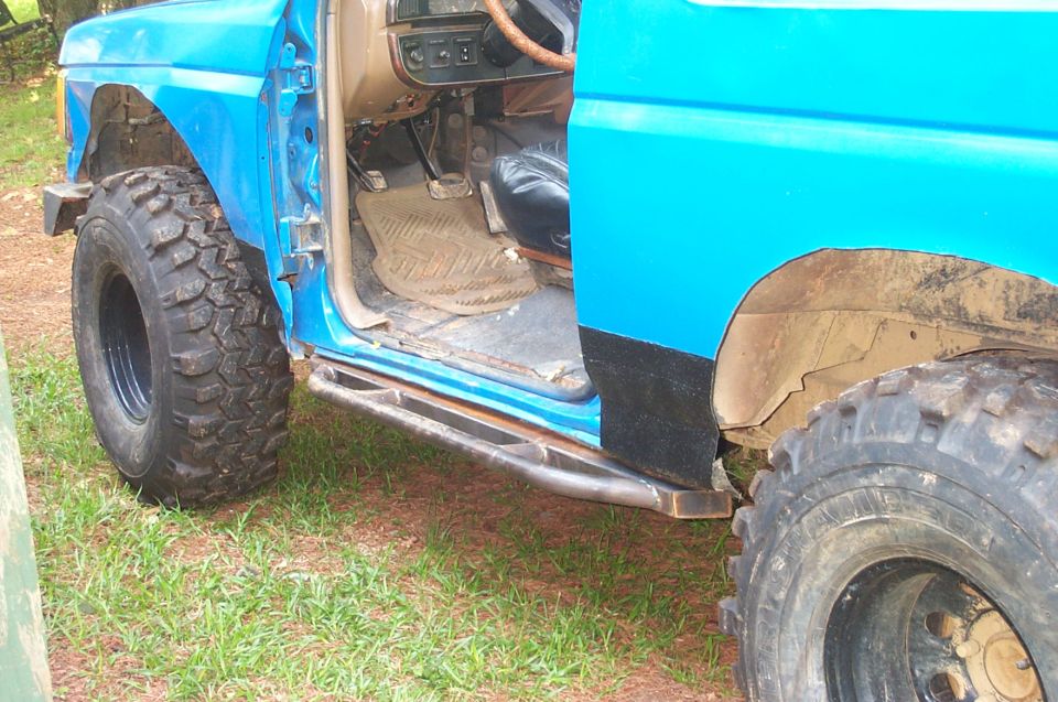 Side view of a blue SUV with door open, showing interior and large off-road tires. Custom metal steps are visible below the door