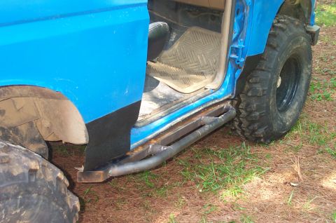 1987 Ford Bronco - Custom metal side steps and large off-road tires are visible on this blue SUV.