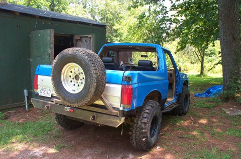 1987 Ford Bronco - Rear view of a blue 1987 Ford Bronco with a spare tire mounted on the custom rear bumper.
