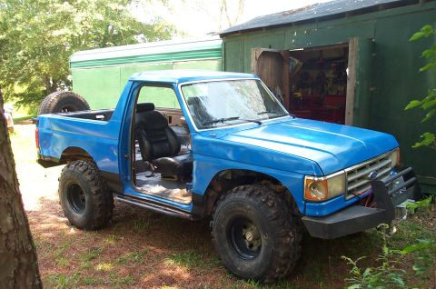 1987 Ford Bronco - This modified blue Ford Bronco is parked outdoors next to a green shed.