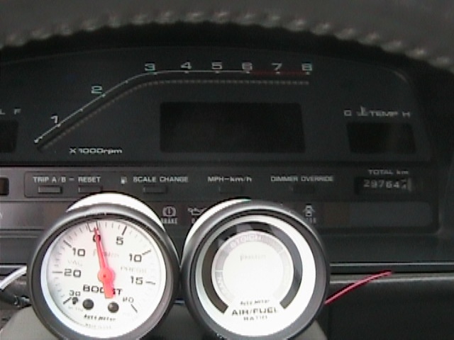 Car dashboard showing tachometer, boost gauge, air/fuel ratio gauge, and odometer reading 29764