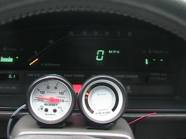 Car dashboard with a digital speedometer showing 0 MPH, a boost gauge, and an air-fuel ratio gauge