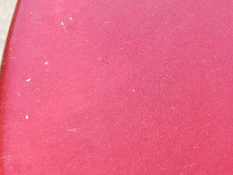 1998 Ford Taurus - A close-up view of a red car's exterior shows minor imperfections and dust specks.