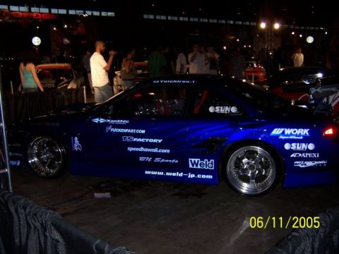 2005 Ford Focus - A highly customized blue sports car is displayed indoors, covered in various sponsor decals and aftermarket parts.