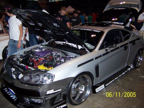 2005 Ford Focus - A silver coupe is displayed with its hood open, revealing a customized engine and various racing decals, with a date stamp of 06/11/2005 vi…