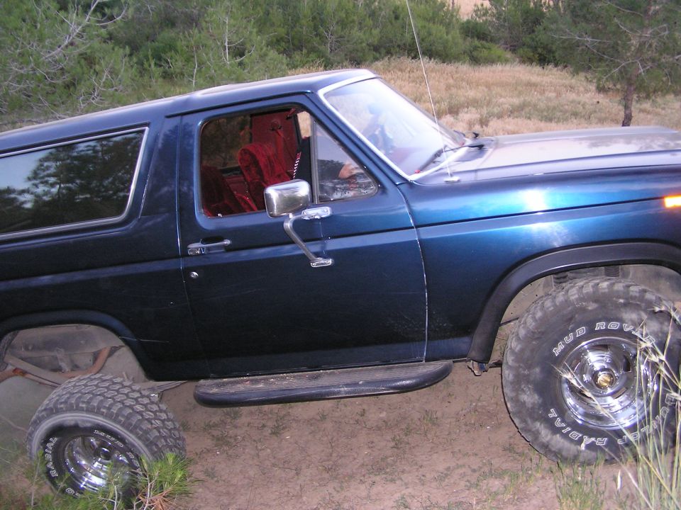 Dark blue Ford Bronco with red interior, side view, off-roading on dirt with tall grass